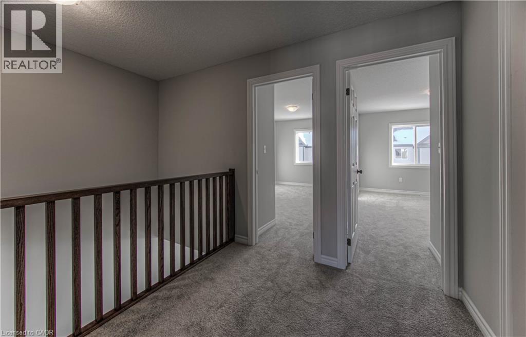 Carpeted hallway featuring a dark wood-finish railing, light grey walls, and two doorways opening into carpeted rooms with windows - 44 Harrison Drive, Cambridge, ON - Indoor Photo Showing Other Room