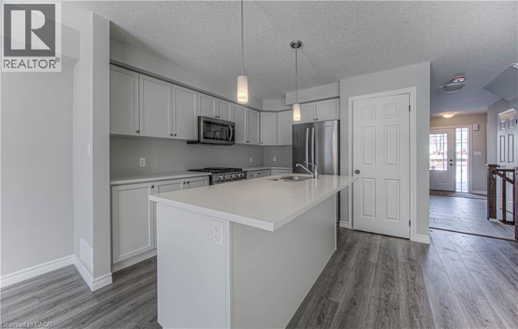 Modern kitchen featuring a central island with an undermount sink, pendant lighting, stainless steel appliances, light gray cabinetry, and wood-finish flooring - 44 Harrison Drive, Cambridge, ON - Indoor Photo Showing Kitchen With Double Sink With Upgraded Kitchen