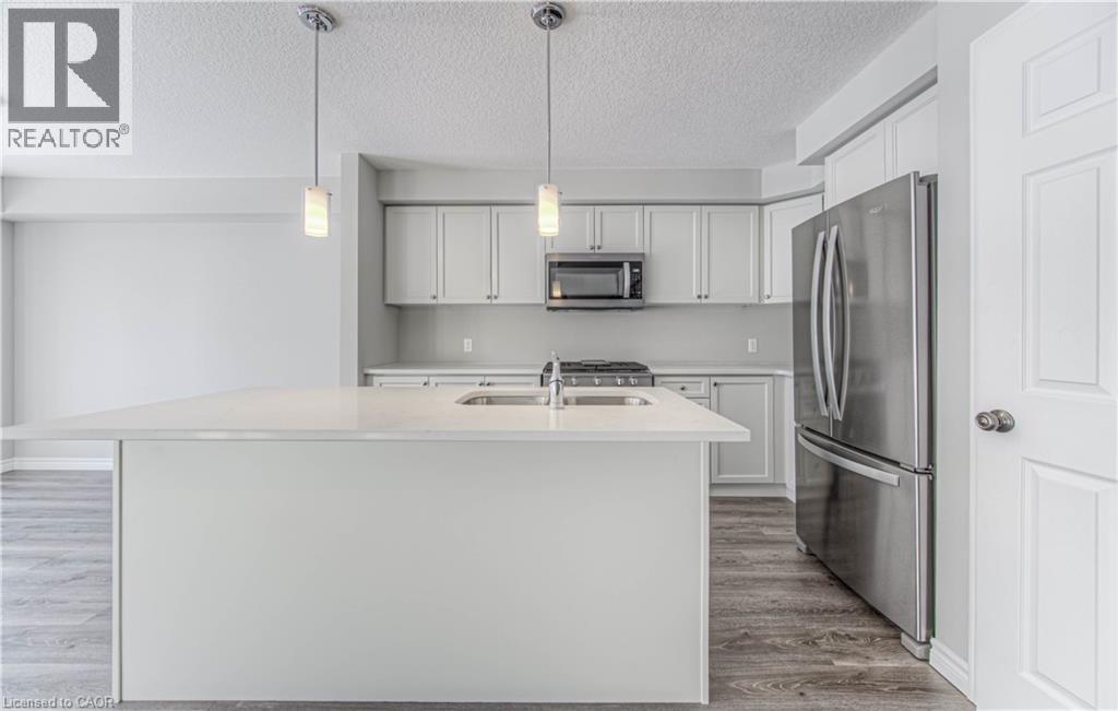 Contemporary kitchen featuring a spacious island with an undermount sink, pendant lighting, stainless steel appliances, white cabinetry, and wood-finish flooring - 44 Harrison Drive, Cambridge, ON - Indoor Photo Showing Kitchen With Stainless Steel Kitchen With Double Sink