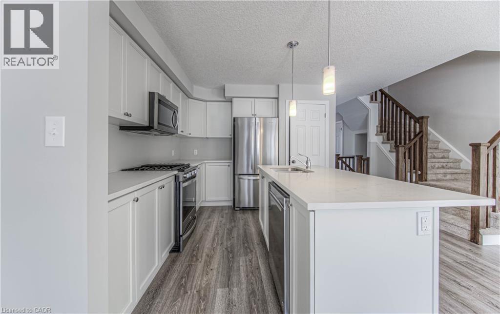 Modern kitchen featuring an extended island with a built-in sink and pendant lighting - 44 Harrison Drive, Cambridge, ON - Indoor Photo Showing Kitchen With Stainless Steel Kitchen With Upgraded Kitchen