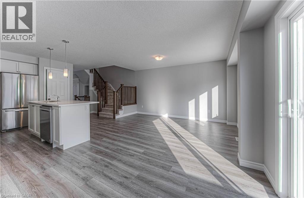 Open-concept living space featuring wood-finish flooring, a kitchen island with pendant lighting, stainless steel appliances, and a staircase with wood railings - 44 Harrison Drive, Cambridge, ON - Indoor Photo Showing Kitchen