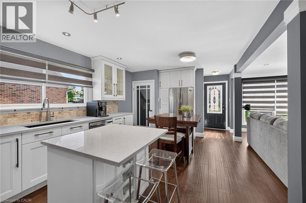 Modern kitchen featuring a central island with a quartz countertop, white cabinetry with dark hardware, stainless steel appliances, and wood-finish flooring - 386 Upper Kenilworth Avenue, Hamilton, ON - Indoor Photo Showing Kitchen