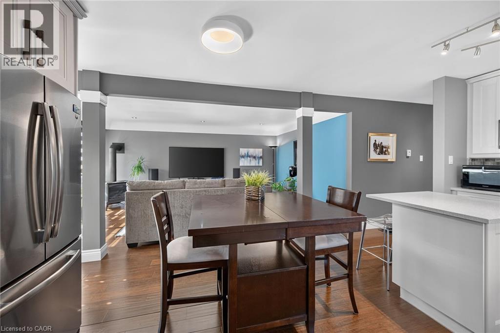 Open-concept living space featuring wood-finish flooring, a stainless steel refrigerator, white shaker-style cabinetry, and a kitchen island with a light-toned countertop - 386 Upper Kenilworth Avenue, Hamilton, ON - Indoor Photo Showing Dining Room