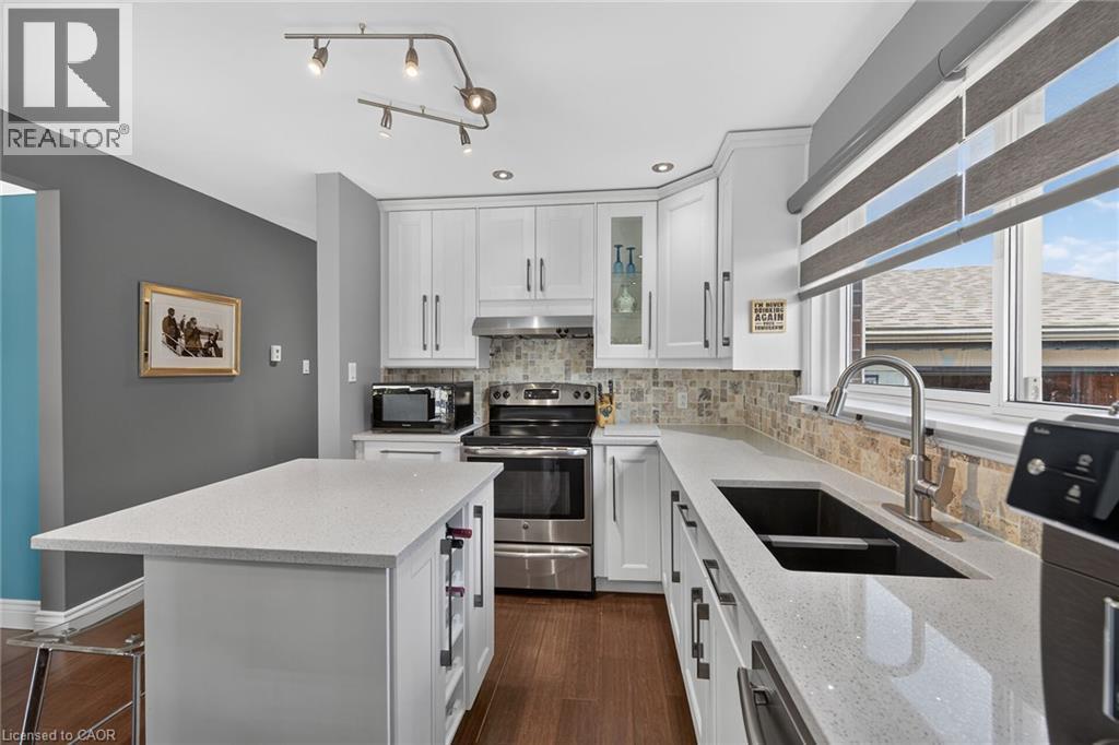 Modern kitchen featuring white cabinetry with brushed nickel hardware, light-toned countertops, wood-finish flooring, a mosaic tile backsplash, and recessed lighting - 386 Upper Kenilworth Avenue, Hamilton, ON - Indoor Photo Showing Kitchen With Stainless Steel Kitchen With Double Sink With Upgraded Kitchen