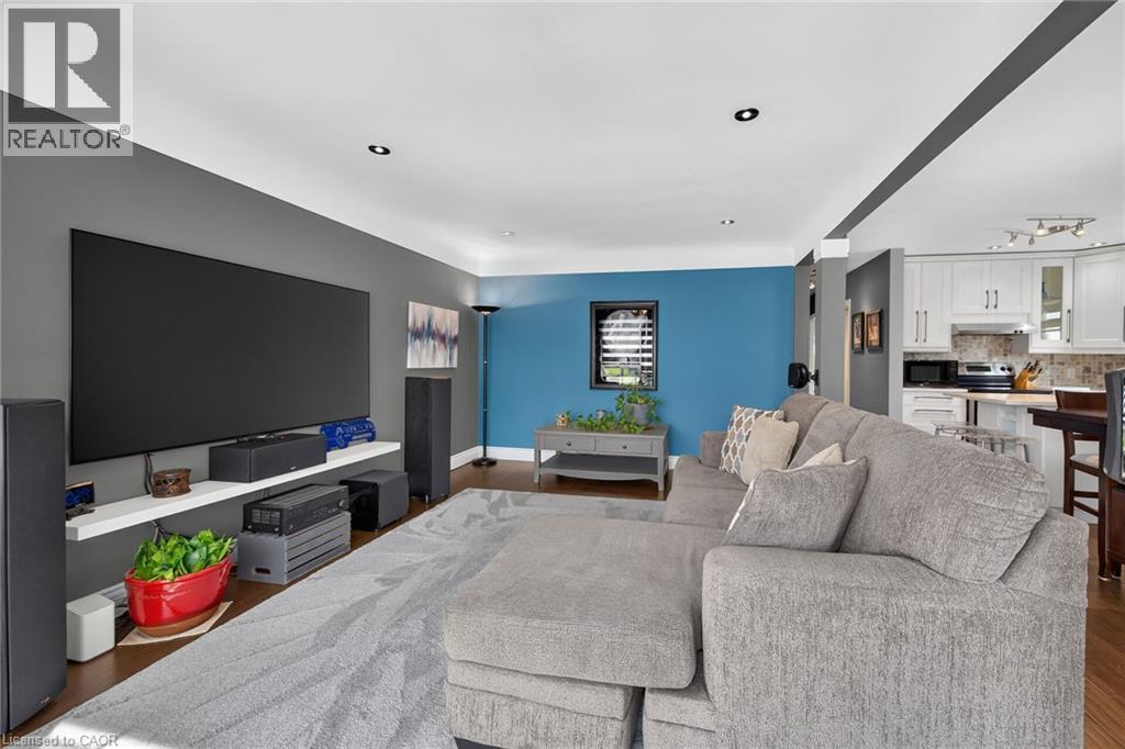 Open-concept living area featuring rich wood-finish flooring, recessed ceiling lighting, and a partial view of the kitchen with white cabinetry and stainless steel appliances - 386 Upper Kenilworth Avenue, Hamilton, ON - Indoor Photo Showing Living Room