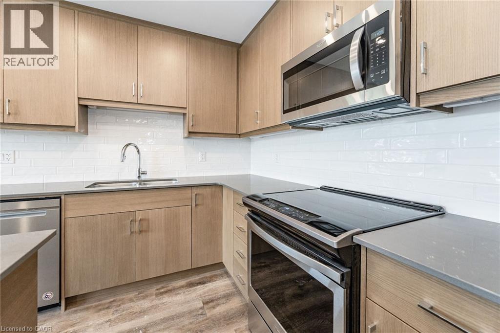 Modern kitchen featuring light wood-finish cabinetry, stainless steel appliances, white subway tile backsplash, gray countertops, and wood-finish flooring - 72 Erb Street E Unit# 103, Waterloo, ON - Indoor Photo Showing Kitchen With Double Sink