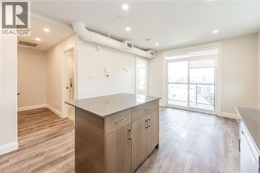 Open-concept living area featuring wood-finish flooring, a kitchen island with stone countertop, modern cabinetry, recessed lighting, and a large sliding glass door with balcony access - 72 Erb Street E Unit# 103, Waterloo, ON - Indoor Photo Showing Other Room