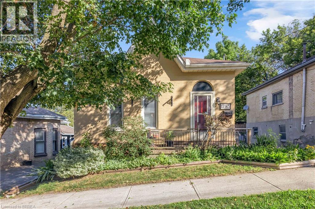 Light-toned brick exterior with an arched entry door and a covered front porch featuring wrought iron railing - 17 Scarfe Avenue, Brantford, ON - Outdoor