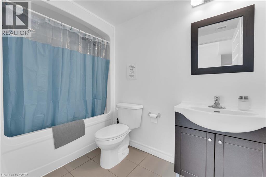 White bathroom featuring a built-in tub with shower, white commode, and a dark wood-finish vanity with an integrated sink - 158 King Street N Unit# 81201, Waterloo, ON - Indoor Photo Showing Bathroom
