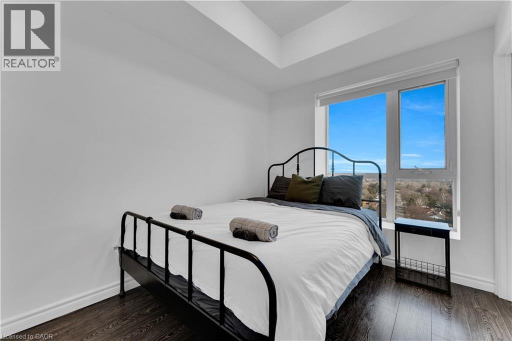 Bright, contemporary bedroom featuring a metal-frame bed, dark wood-finish flooring, and floor-to-ceiling windows with expansive natural light and clear sky views - 158 King Street N Unit# 81201, Waterloo, ON - Indoor Photo Showing Bedroom