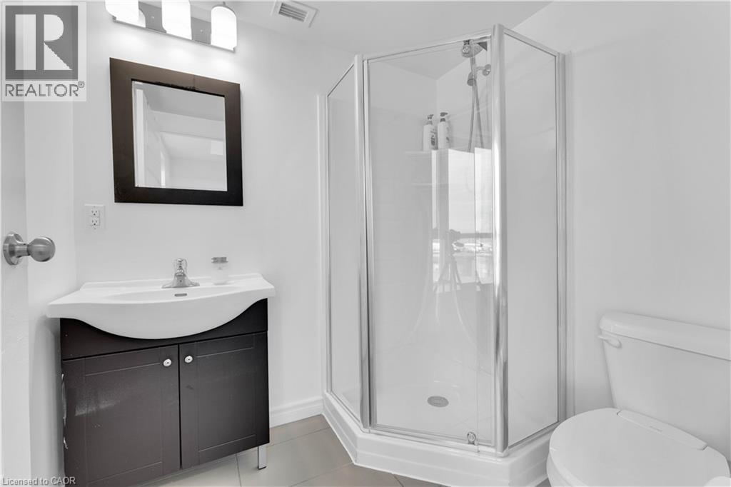Modern bathroom featuring a corner glass-enclosed shower with chrome fixtures, sleek black vanity with dual cabinet storage and white curved sink, framed mirror, white subway tile walls, and ceramic t - 158 King Street N Unit# 81201, Waterloo, ON - Indoor Photo Showing Bathroom