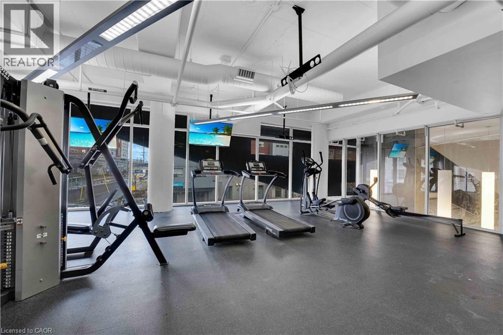 Dedicated fitness center featuring resilient flooring, exposed ductwork, large windows, recessed and suspended lighting, and mounted screens - 158 King Street N Unit# 81201, Waterloo, ON - Indoor Photo Showing Gym Room