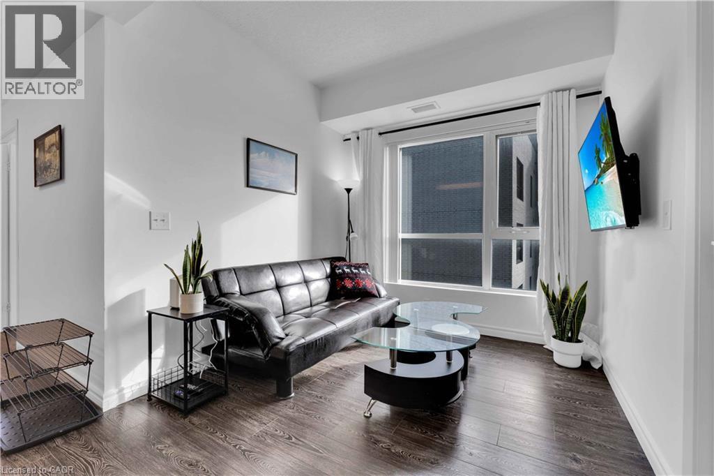 Living area featuring wood-finish flooring, a large window with white curtains, and a wall-mounted flat-screen display - 158 King Street N Unit# 81201, Waterloo, ON - Indoor Photo Showing Living Room