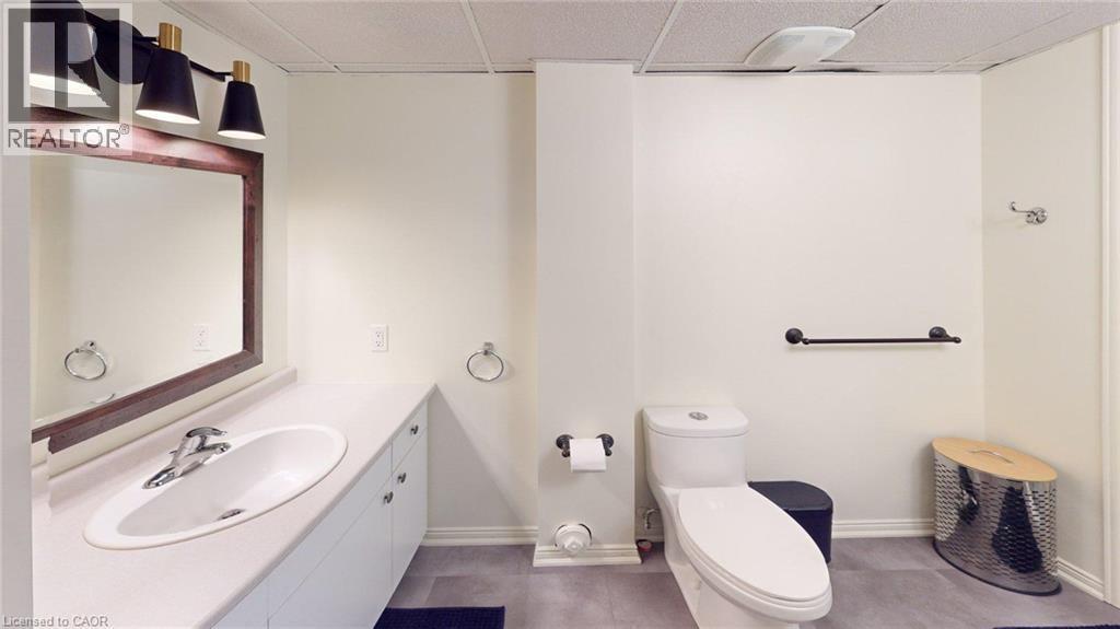 Bathroom featuring a single vanity with an oval basin, a dark wood-framed mirror, and a three-light fixture with black conical shades - 4101 Diana Park, Vineland, ON - Indoor Photo Showing Bathroom