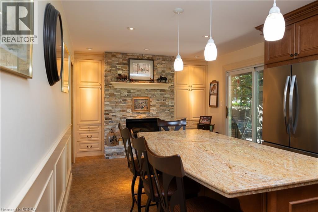 Spacious kitchen featuring a large island with a stone countertop, a stone-clad fireplace with a mantle, recessed lighting, pendant lights, and built-in cabinetry - 269 Brant County Road 22, Ancaster, ON