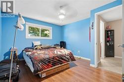 Bedroom featuring wood-finish flooring, a white trim window, and a ceiling fan with integrated lighting -