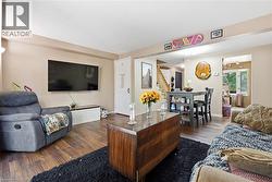 Open-concept living space featuring a wood-finish flooring throughout, wall-mounted flat-screen television, and a dark wood centerpiece table -