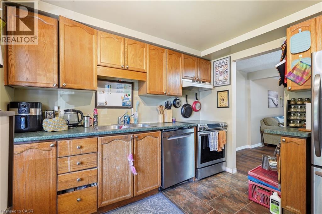 Warm wood cabinetry and stainless steel appliances define this functional kitchen, featuring ample storage with upper and lower cabinetry, a gas range, and a ceramic tile backsplash - 292 Mayview Court Unit# B, Waterloo, ON - Indoor Photo Showing Kitchen