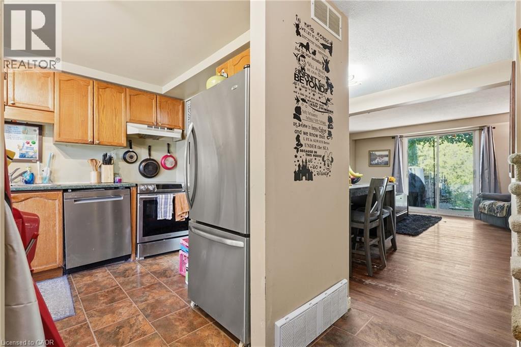 Open-concept kitchen and living area featuring stainless steel appliances, wood cabinetry, wood-finish flooring, and abundant natural light from multiple windows - 292 Mayview Court Unit# B, Waterloo, ON - Indoor Photo Showing Kitchen