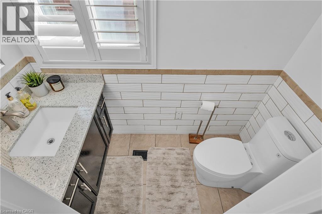White subway tile wainscoting with a tan border accents this bathroom, featuring a white porcelain toilet - 73 Fitzgerald Drive, Cambridge, ON - Indoor Photo Showing Bathroom