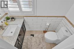 White subway tile wainscoting with a tan border accents this bathroom, featuring a white porcelain toilet -