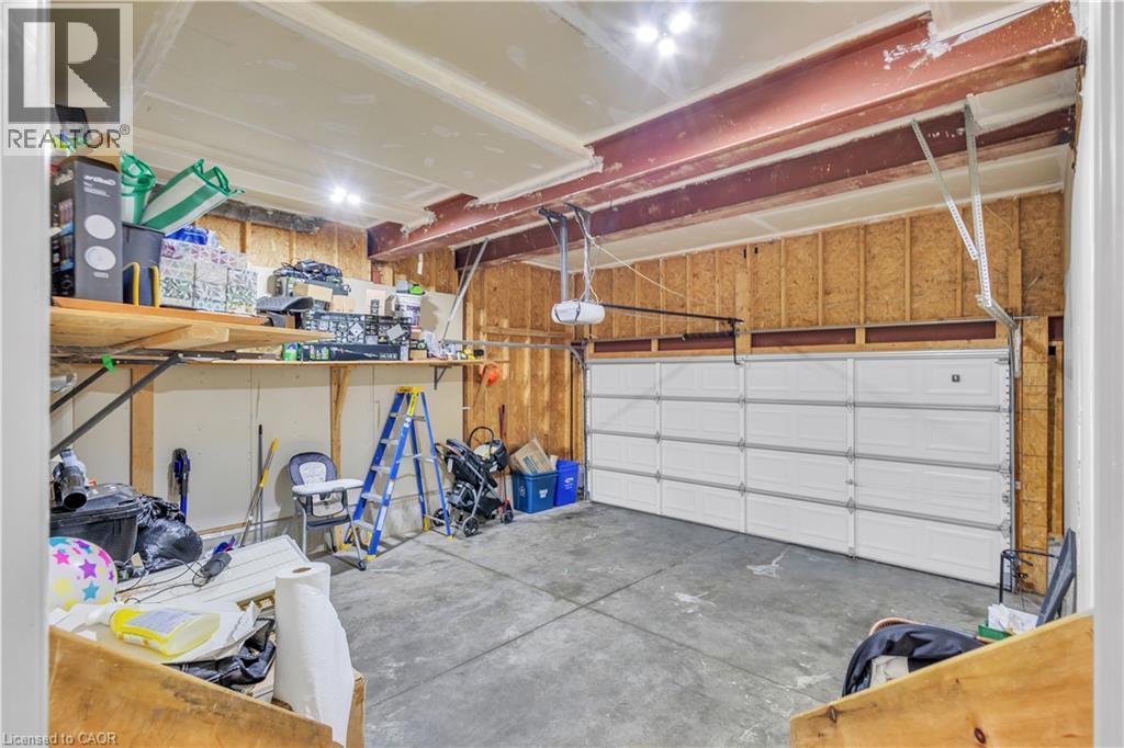 Garage space featuring a paneled overhead door, concrete flooring, exposed wood framing, and an overhead storage shelf - 73 Fitzgerald Drive, Cambridge, ON - Indoor Photo Showing Garage