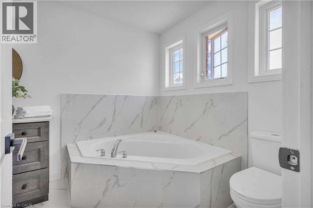 Corner soaking tub with polished chrome fixtures, surrounded by marble-look tile - 73 Fitzgerald Drive, Cambridge, ON - Indoor Photo Showing Bathroom