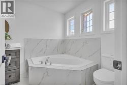 Corner soaking tub with polished chrome fixtures, surrounded by marble-look tile -