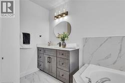 Bathroom featuring a wood-finish vanity with a light-colored countertop, an irregular shaped mirror, and overhead vanity lighting -