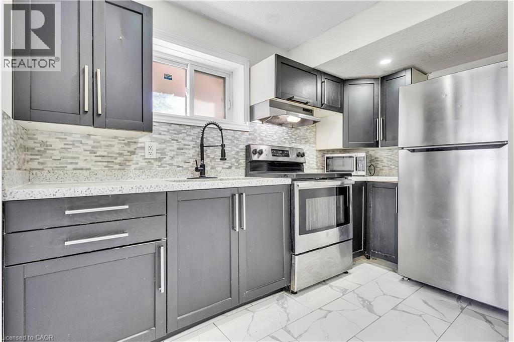 Modern kitchen featuring dark cabinetry with brushed nickel hardware, white stone-finish countertops, and a mosaic tile backsplash - 73 Fitzgerald Drive, Cambridge, ON - Indoor Photo Showing Kitchen With Upgraded Kitchen