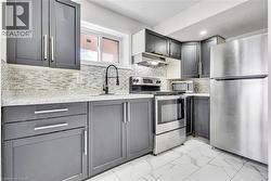 Modern kitchen featuring dark cabinetry with brushed nickel hardware, white stone-finish countertops, and a mosaic tile backsplash -