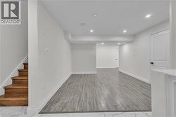 Spacious lower-level area featuring recessed lighting, wood-finish flooring, white baseboards, and a bright white door with dark hardware -