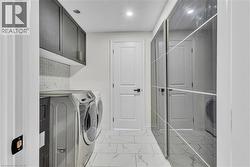 Laundry area featuring a tile backsplash, dark cabinetry, and white flooring -