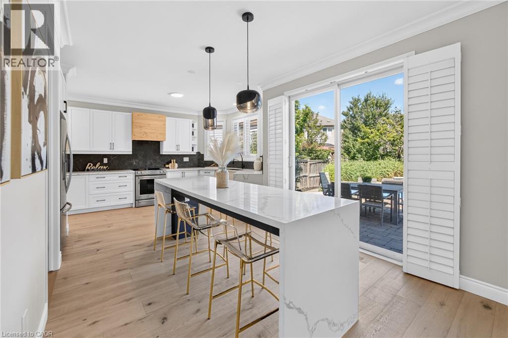 Bright kitchen featuring light wood-finish flooring, white cabinetry, dark stone backsplash, and a large central island with a light-colored countertop - 1533 Morse Place, Milton, ON - Indoor Photo Showing Kitchen With Upgraded Kitchen