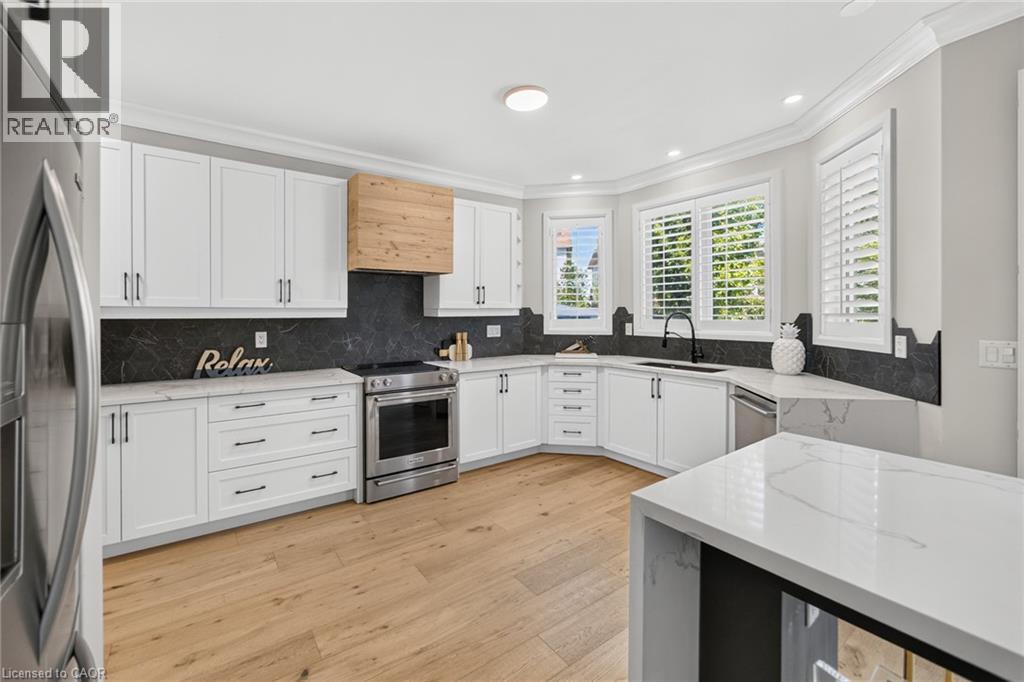 Modern kitchen featuring white shaker cabinetry, stainless steel appliances, a wood-finish range hood, and light wood-finish flooring - 1533 Morse Place, Milton, ON - Indoor Photo Showing Kitchen