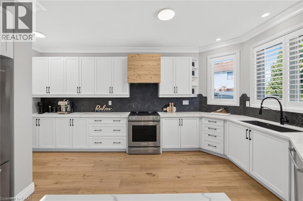 White shaker cabinetry with matte black hardware, light wood-finish flooring, a wood-wrapped range hood, and dark stone backsplash - 1533 Morse Place, Milton, ON - Indoor Photo Showing Kitchen