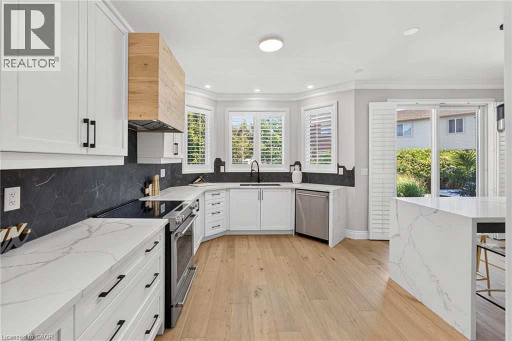 Modern kitchen featuring white shaker cabinetry, stainless steel appliances, a wood-finish range hood, black hexagonal tile backsplash, and light wood-finish flooring - 1533 Morse Place, Milton, ON - Indoor Photo Showing Kitchen With Upgraded Kitchen
