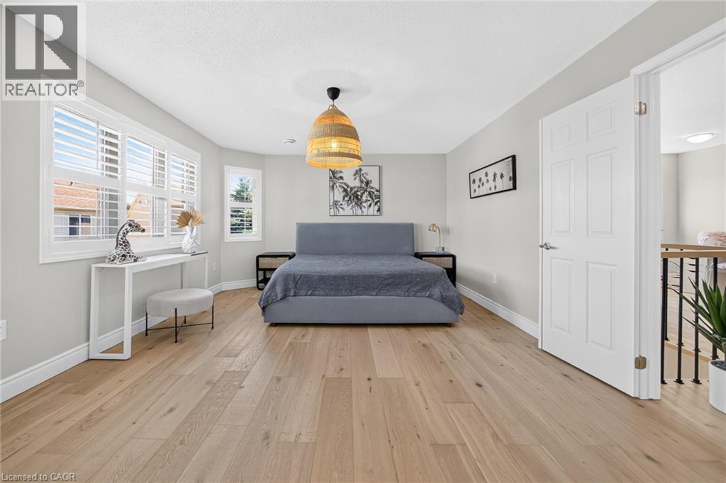 Spacious room featuring light wood-finish flooring, multiple windows with white plantation shutters, and a woven pendant light fixture - 1533 Morse Place, Milton, ON - Indoor