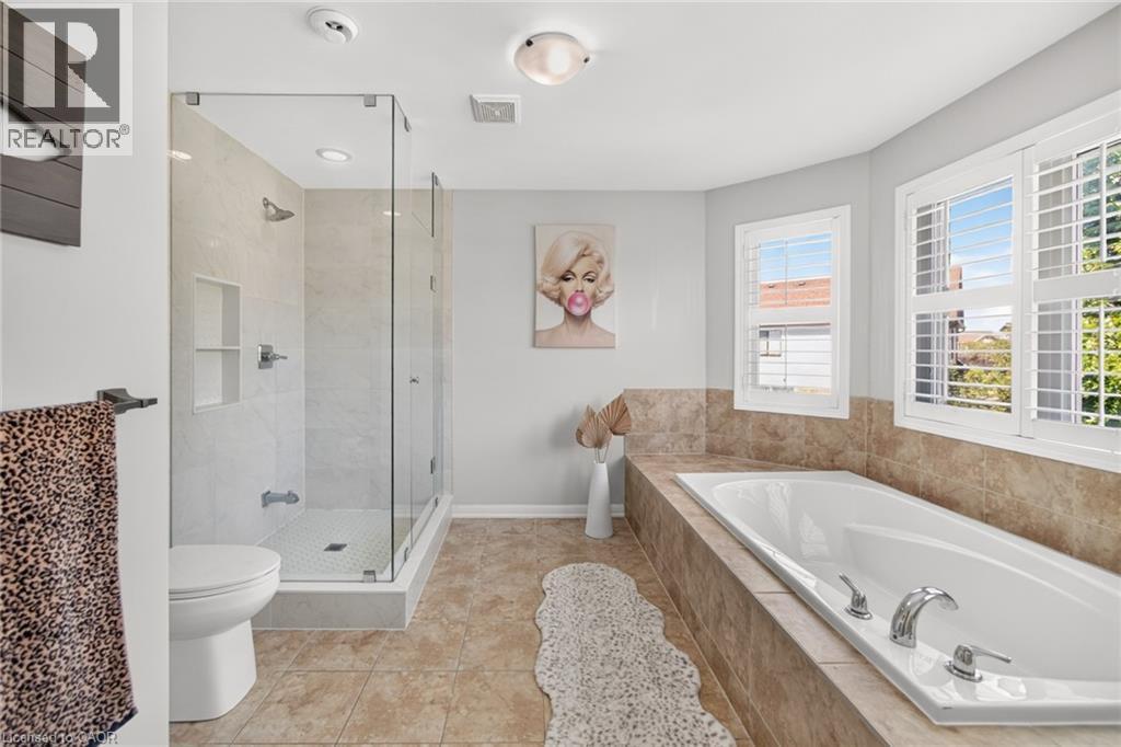 Spa-inspired primary bathroom featuring a frameless glass-enclosed shower with tile surround, a soaking tub with chrome fixtures, dual vanity, heated floor, travertine-finish tile flooring, and abunda - 1533 Morse Place, Milton, ON - Indoor Photo Showing Bathroom