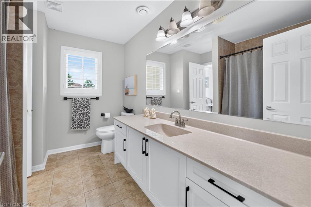 Spacious bathroom featuring a long vanity with dual sinks, a large integrated mirror, and white cabinetry with matte black hardware - 1533 Morse Place, Milton, ON - Indoor Photo Showing Bathroom