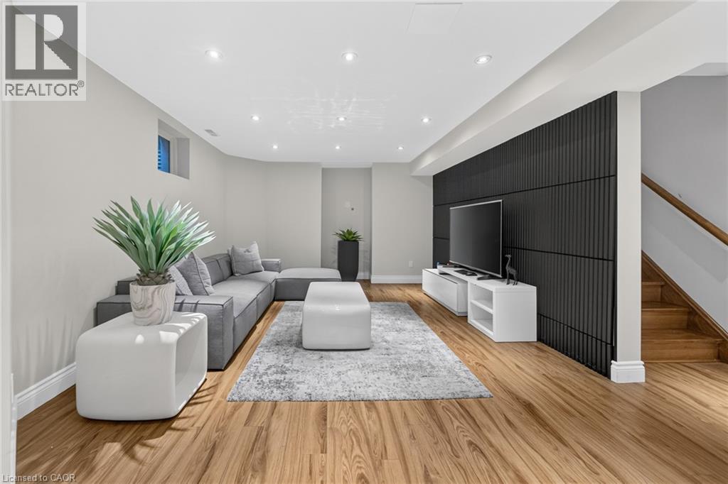 Spacious living area featuring wood-finish flooring, recessed lighting, a built-in media wall with vertical paneling, and a wood staircase with a handrail - 1533 Morse Place, Milton, ON - Indoor Photo Showing Other Room
