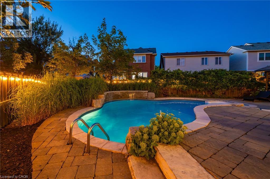Curved inground pool featuring a waterfall, stone coping, and integrated lighting - 1533 Morse Place, Milton, ON - Outdoor With In Ground Pool With Backyard