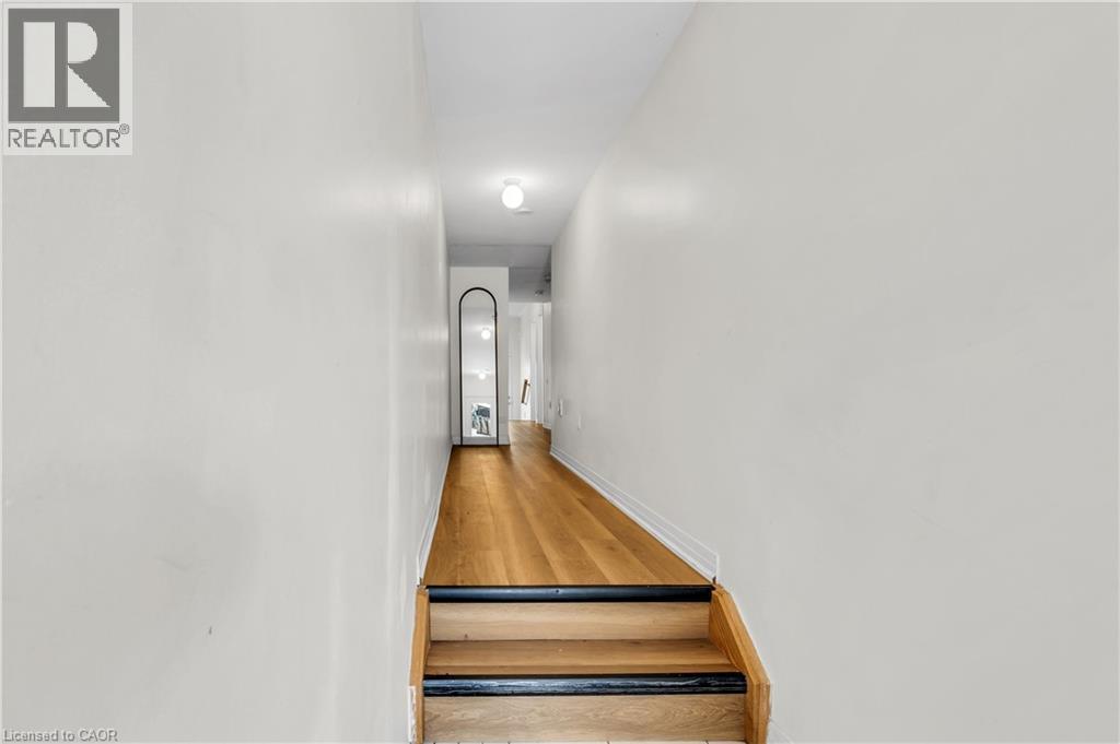 Staircase entry featuring natural wood treads with black nosing, leading to a hallway with wood-finish flooring and light-toned walls - 1451 Green Road, Bowmanville, ON - Indoor Photo Showing Other Room