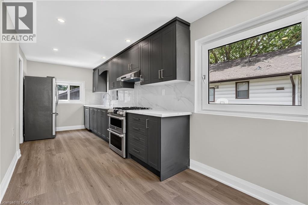 Modern kitchen featuring dark cabinetry, stainless steel appliances, white countertops, and a full-height tile backsplash - 36 Mahony Avenue, Hamilton, ON - Indoor Photo Showing Kitchen