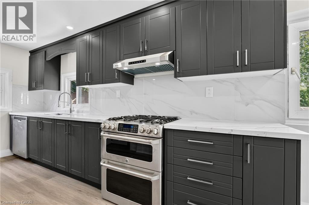 Modern kitchen featuring dark cabinetry, white countertops, a stainless steel range with a double oven, a matching range hood, and a white tile backsplash - 36 Mahony Avenue, Hamilton, ON - Indoor Photo Showing Kitchen With Upgraded Kitchen