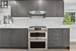 Contemporary kitchen featuring dark gray shaker cabinetry, white countertops, and a white tile backsplash with subtle veining -