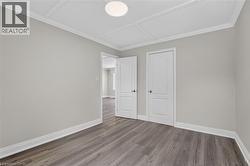 Spacious interior room featuring wood-finish flooring, light gray wall tones, white baseboards, and white crown molding -