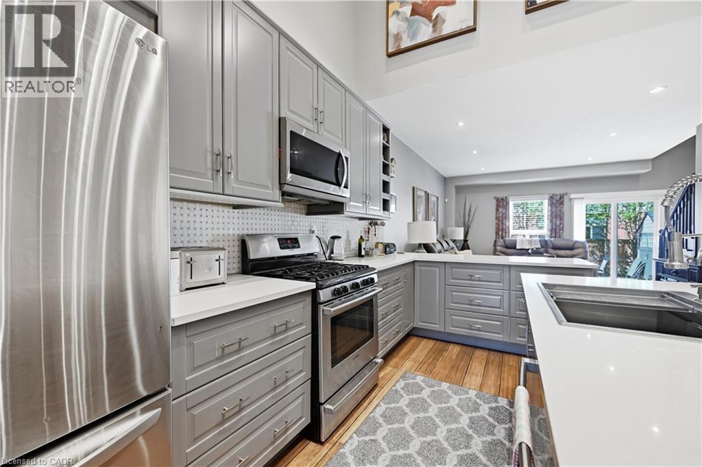 Open-concept kitchen featuring light gray cabinetry, white countertops, stainless steel appliances, and wood-finish flooring - 10 Kopperfield Lane, Hamilton, ON - Indoor Photo Showing Kitchen With Upgraded Kitchen