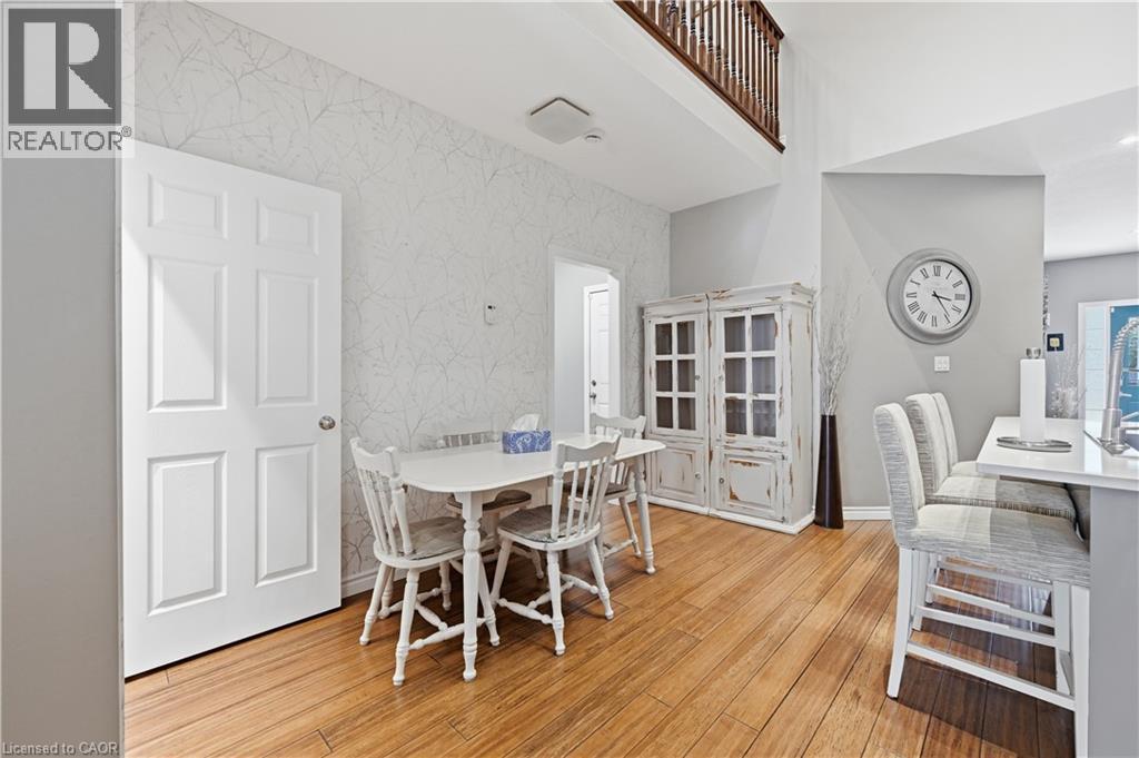 Open-concept dining area featuring wood-finish flooring, a white six-panel door, and a built-in breakfast bar with upholstered stools - 10 Kopperfield Lane, Hamilton, ON - Indoor Photo Showing Dining Room