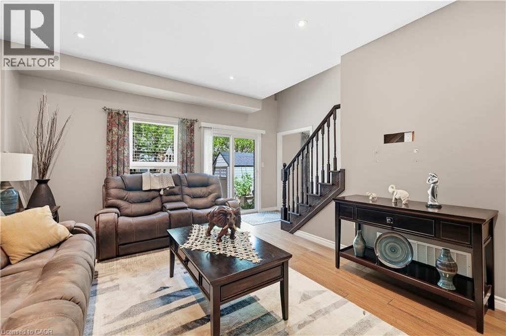 Open living space featuring wood-finish flooring, recessed lighting, and a prominent staircase with dark wood railings - 10 Kopperfield Lane, Hamilton, ON - Indoor Photo Showing Living Room